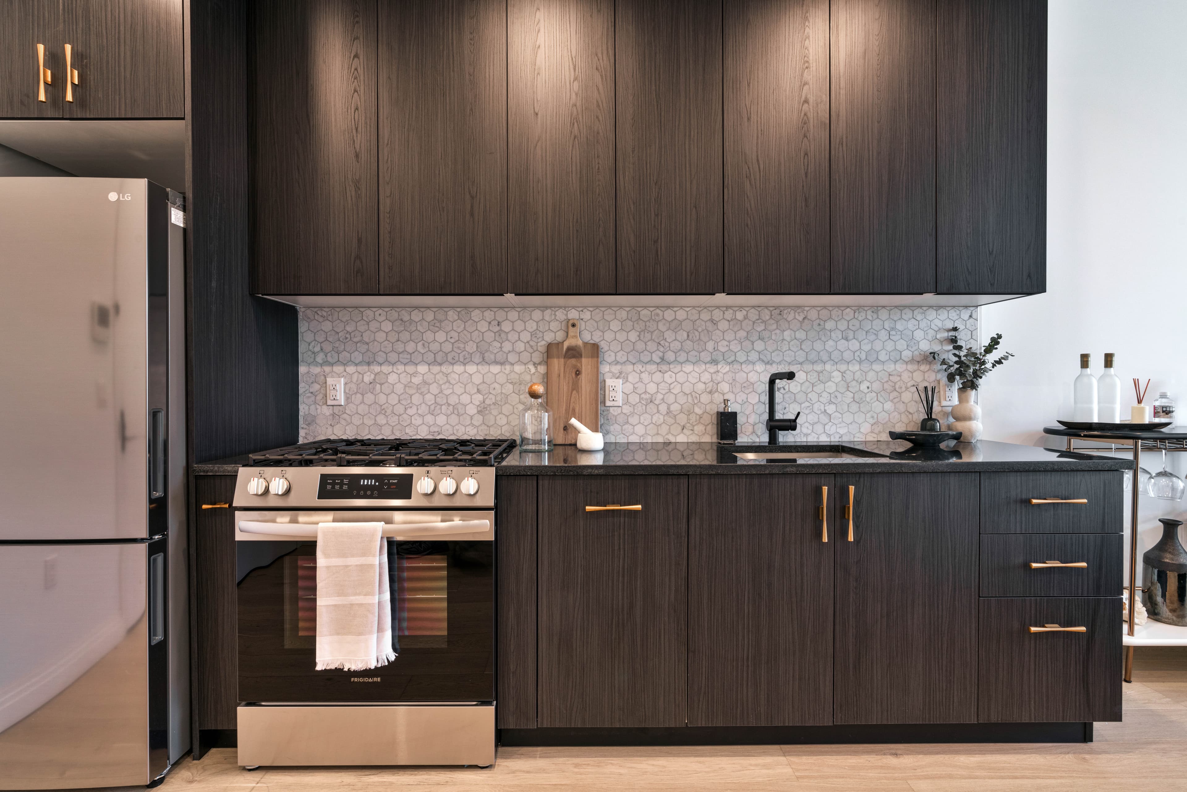 The kitchen of a residence at 875 Fourth Avenue with dark cabinetry, a marble hex backsplash and stainless steel appliances