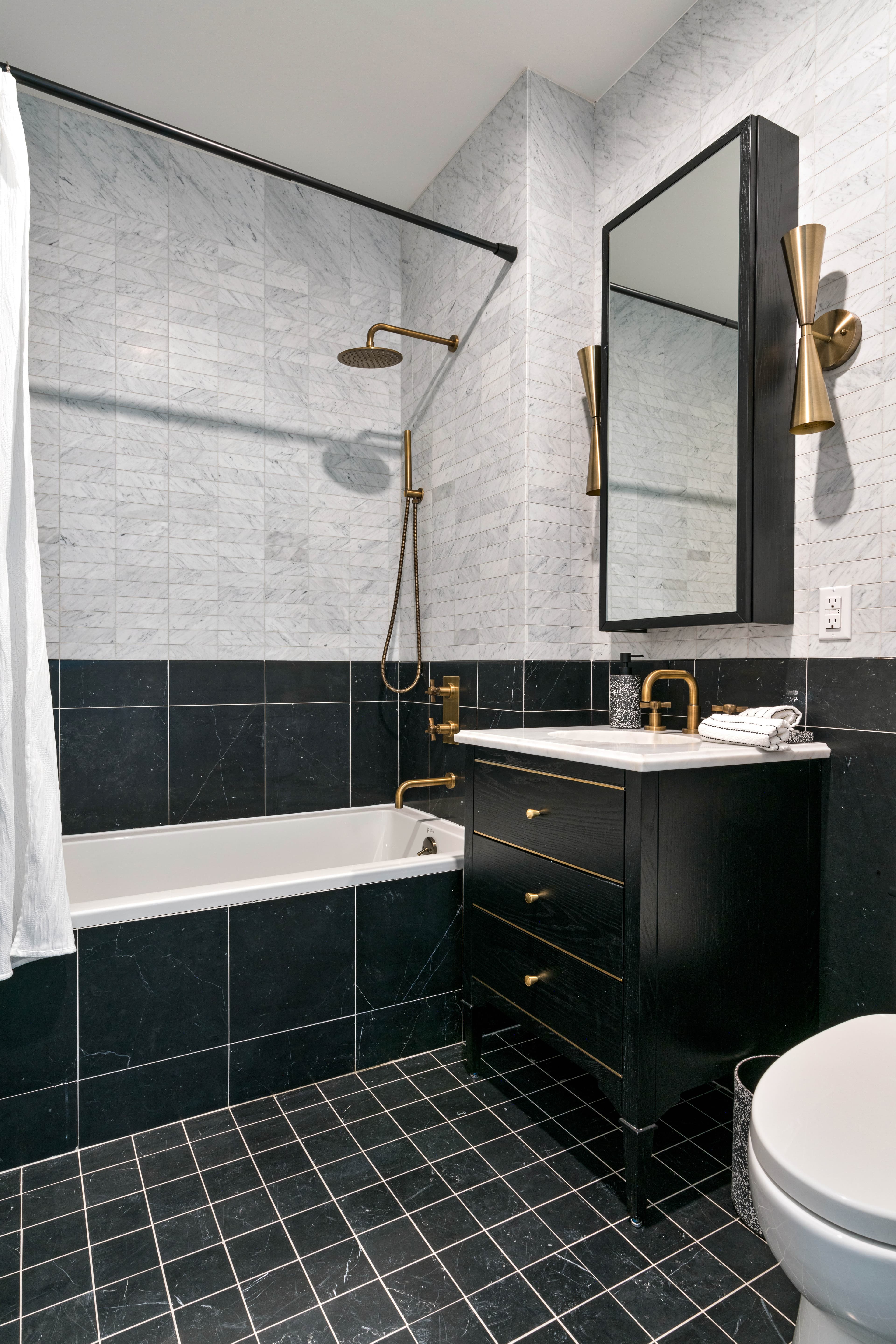 A residence bathroom at 875 Fourth Avenue with marble tiling, a tub with a rain shower and brushed brass fixtures