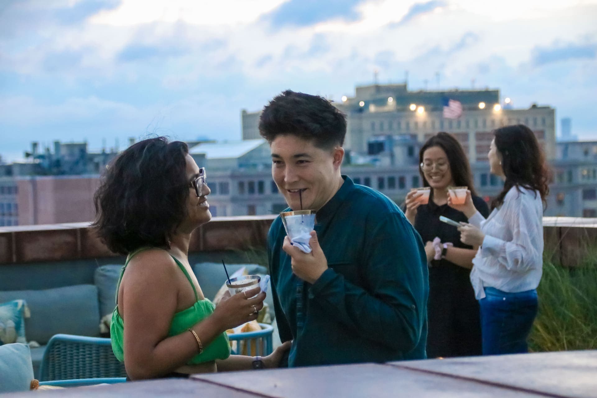 Two residents laughing over drinks as the evening light fades on the rooftop at 875 Fourth Avenue