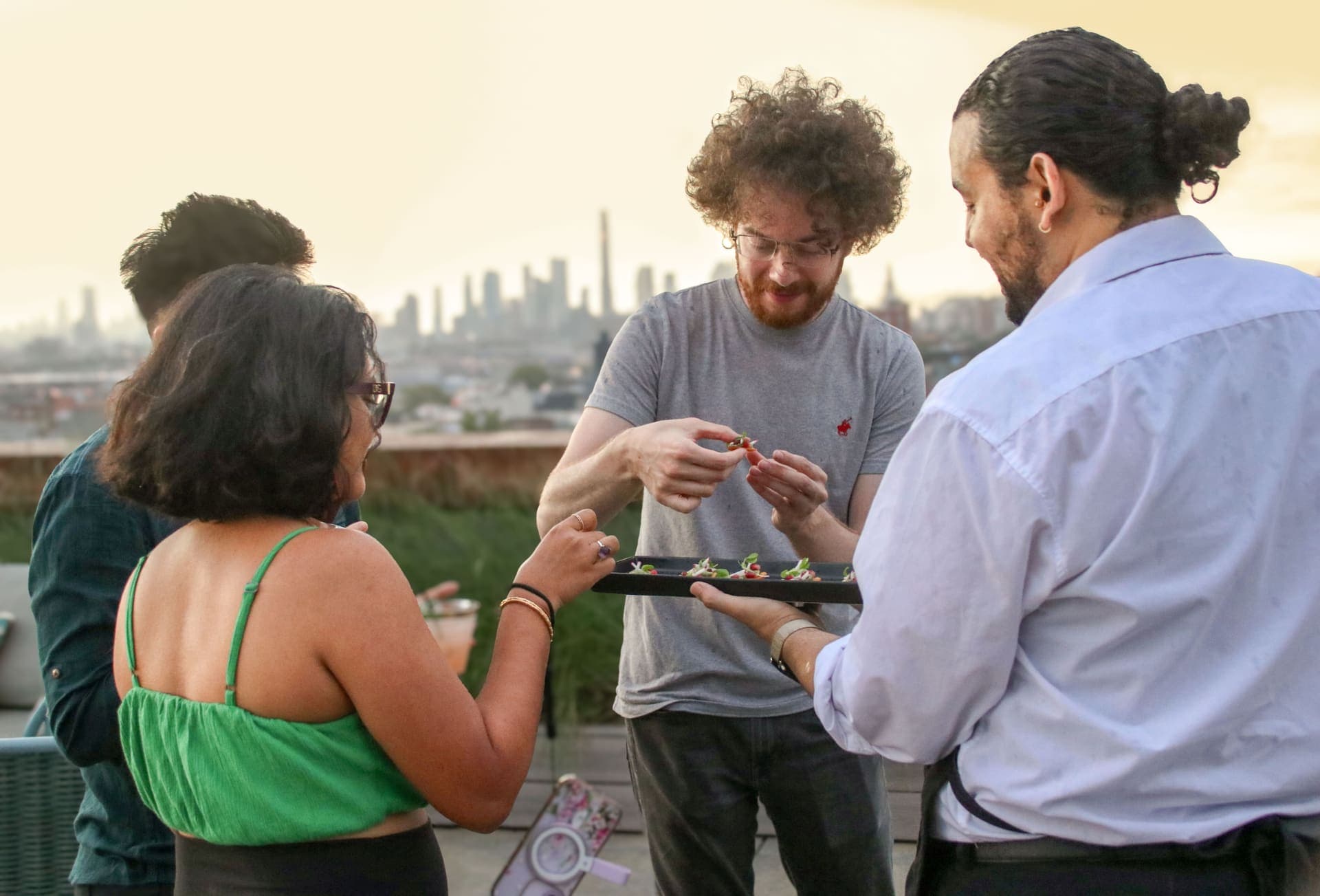 A server offering a tray of appetizers to guests standing at the terrace railing at 875 Fourth Avenue