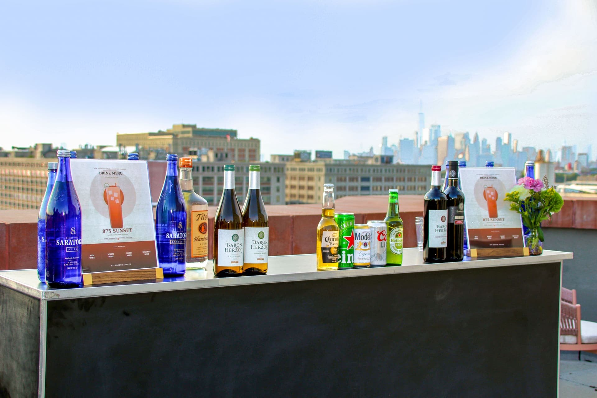 The rooftop bar set with the evening drink menu and the Manhattan skyline beyond at 875 Fourth Avenue