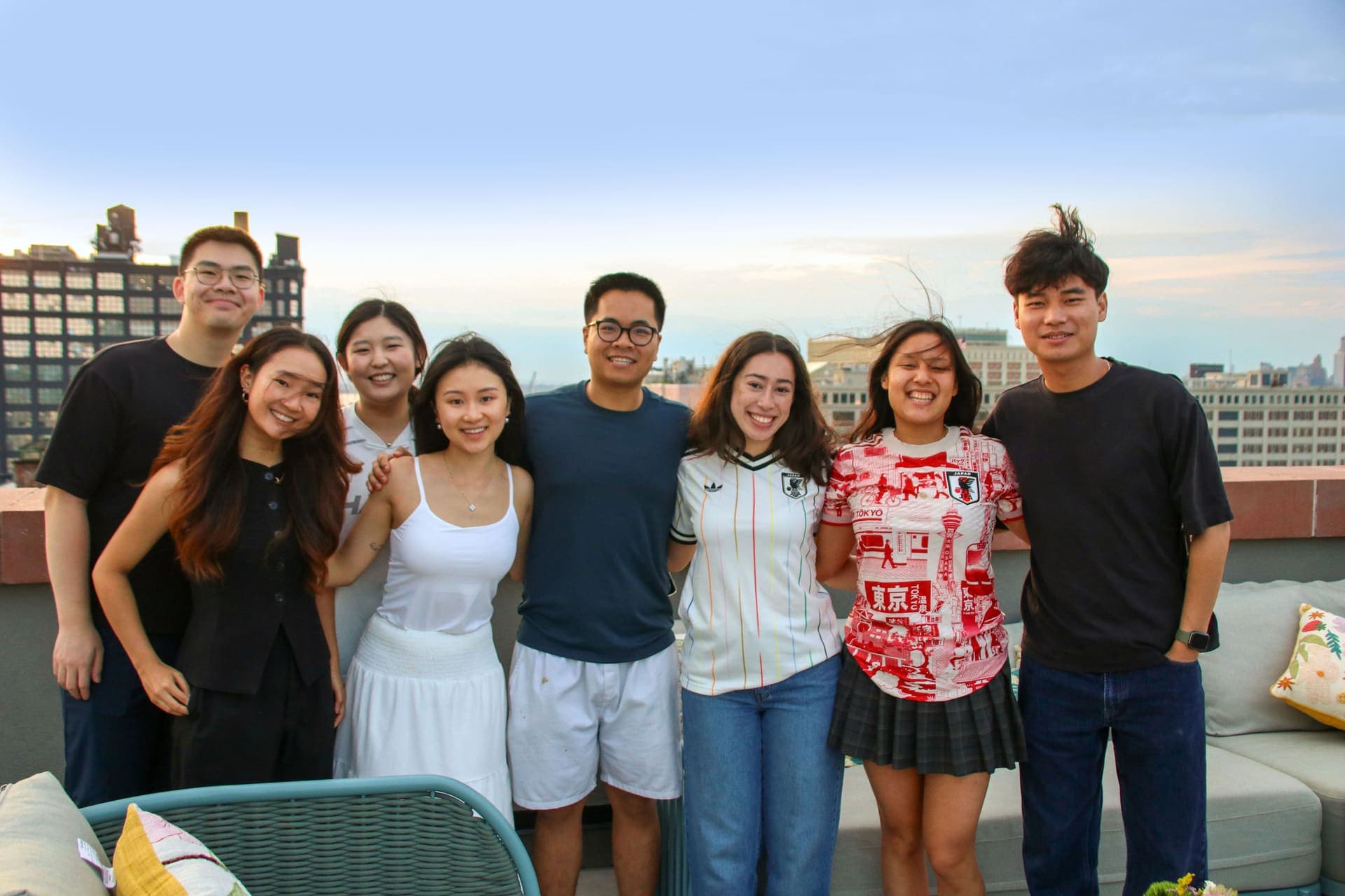 An eight-person group of friends together for a photo on the rooftop terrace at 875 Fourth Avenue with the skyline behind