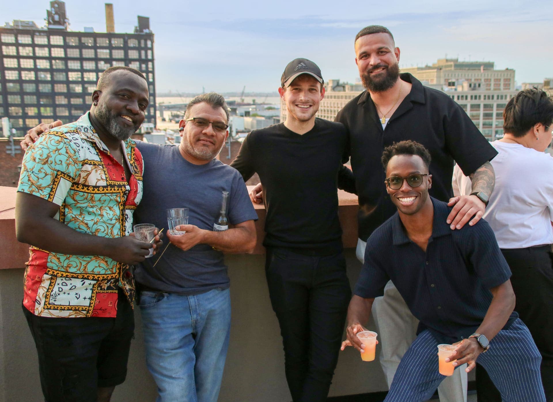 A larger group gathering for a photo with the Manhattan skyline behind on the rooftop at 875 Fourth Avenue