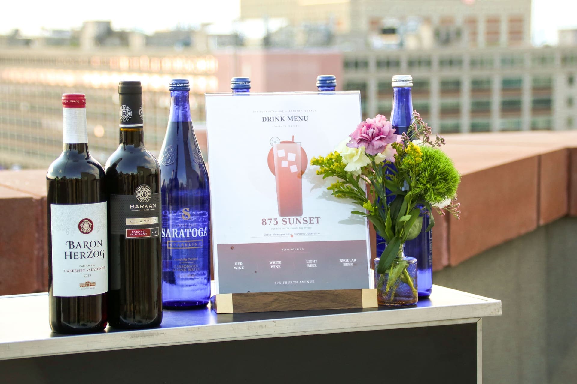 The evening cocktail menu styled with fresh flowers on the rooftop terrace at 875 Fourth Avenue