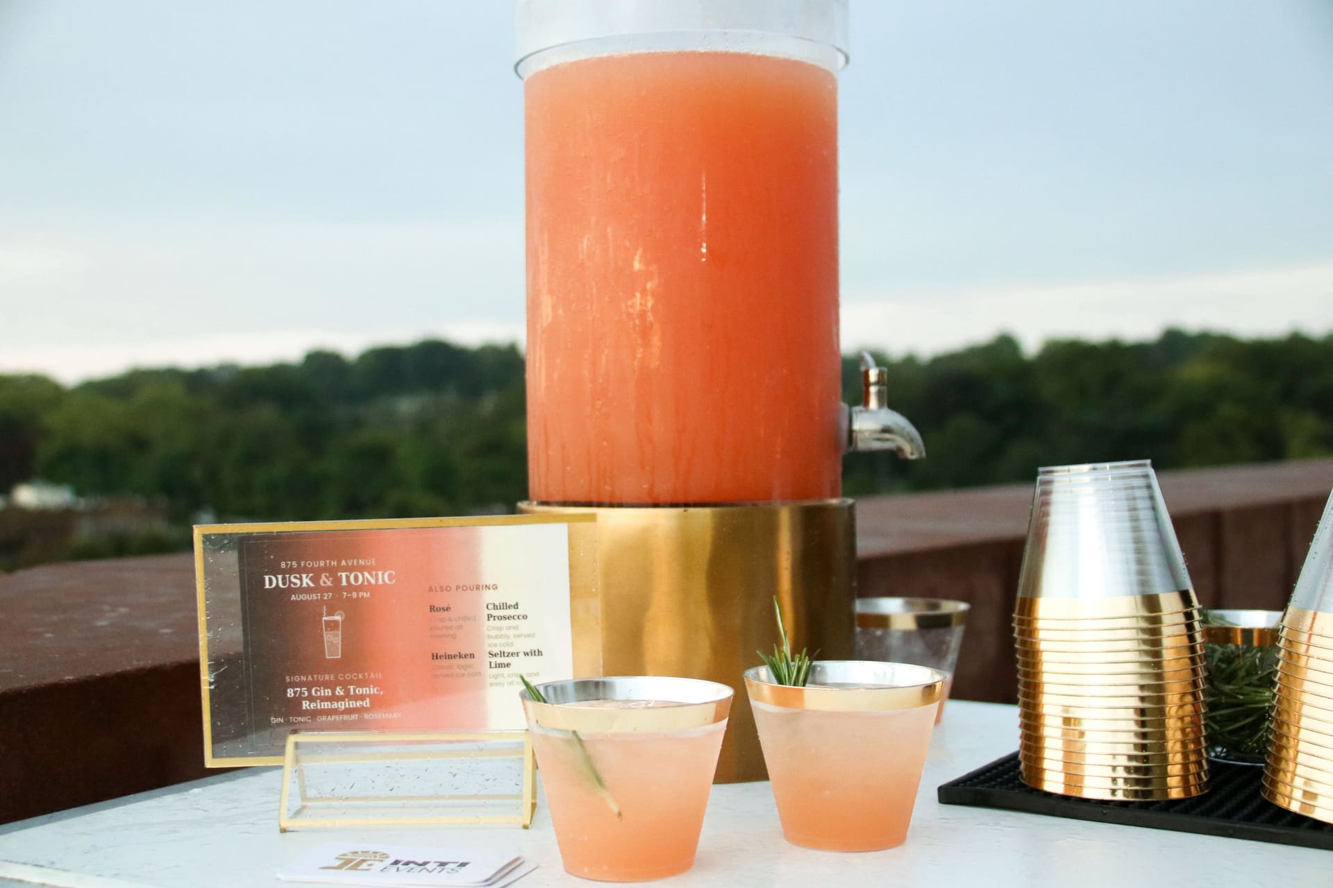 The Dusk and Tonic cocktail station with the printed evening menu and gold-rimmed glasses on the rooftop terrace at 875 Fourth Avenue