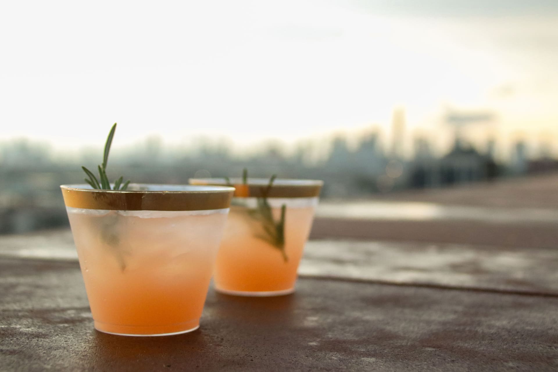 Two gold-rimmed cocktails garnished with rosemary resting on the terrace parapet at 875 Fourth Avenue