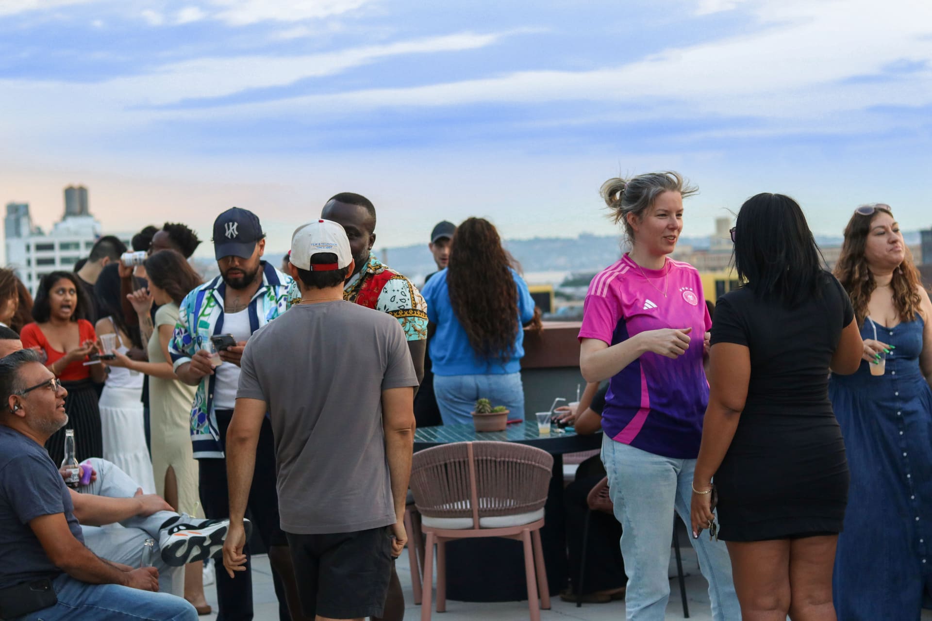 A large group gathered on the rooftop terrace at dusk as the skyline lights up at 875 Fourth Avenue